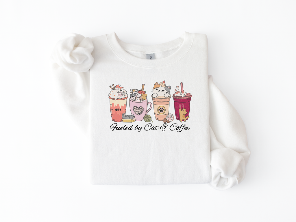 White crewneck sweatshirt flat lay with cat-themed lattes and Fueled by Cats & Coffee