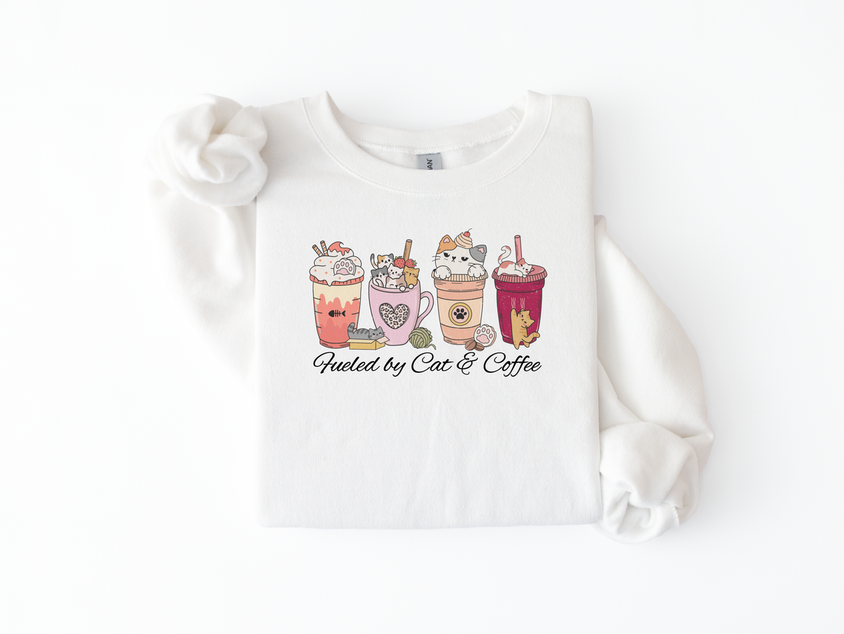White crewneck sweatshirt flat lay with cat-themed lattes and Fueled by Cats & Coffee