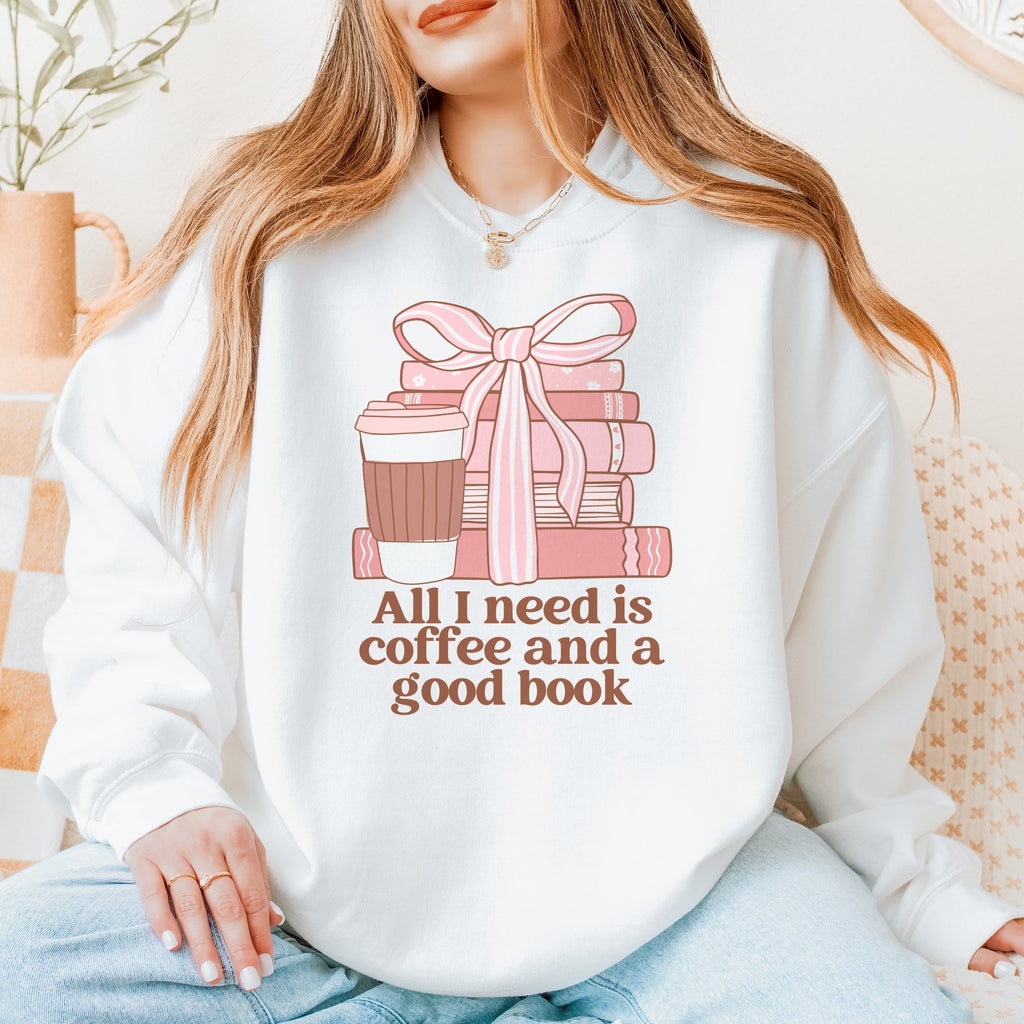 Woman wearing a white sweatshirt with pink books, a coffee cup and a bow reading All I need is coffee and a good book