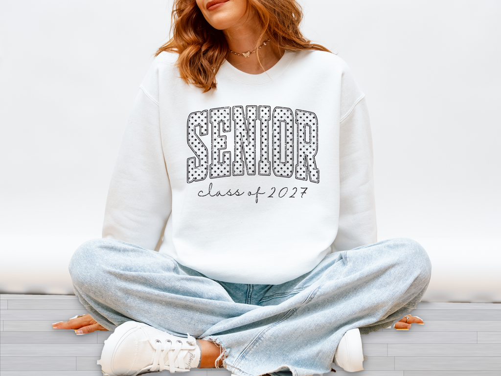 Woman wearing a white sweatshirt with polka dot SENIOR varsity letters and Class of 2027