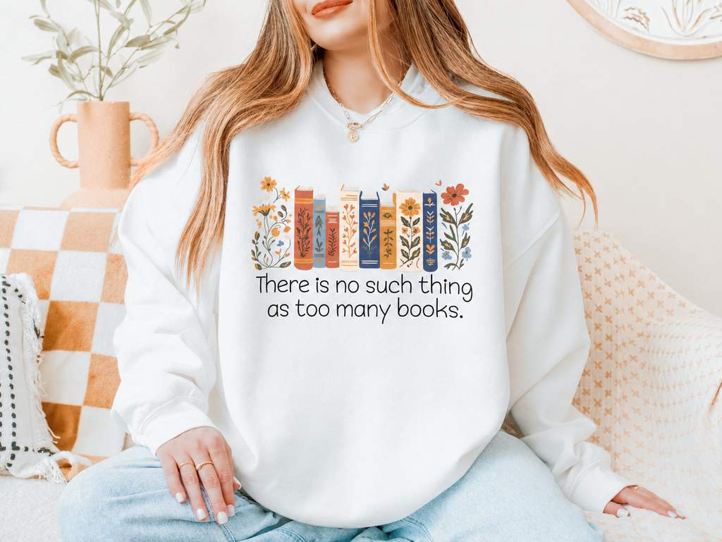 Woman wearing a white sweatshirt with floral book spines and the words There is no such thing as too many books