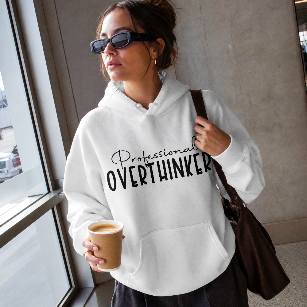 Woman holding a coffee wearing a white top that reads Professional Overthinker
